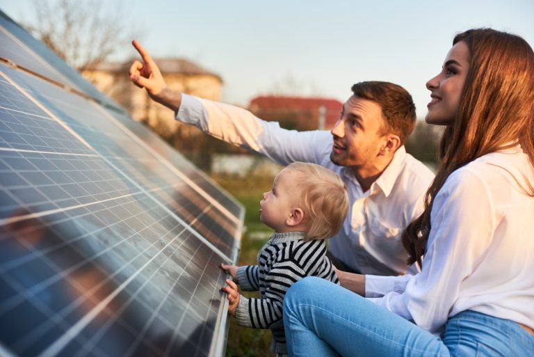 Man Shows His Family The Solar Panels On The Plot Near The House During A Warm Day