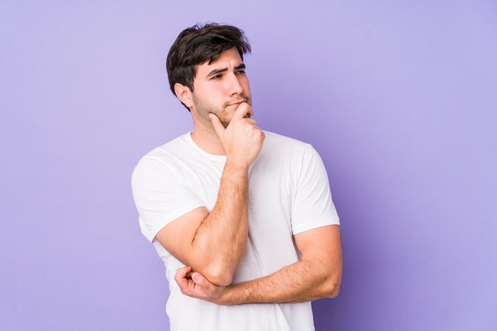 Young Man Isolated On Purple Background Looking Sideways With Doubtful And Skeptical Expression